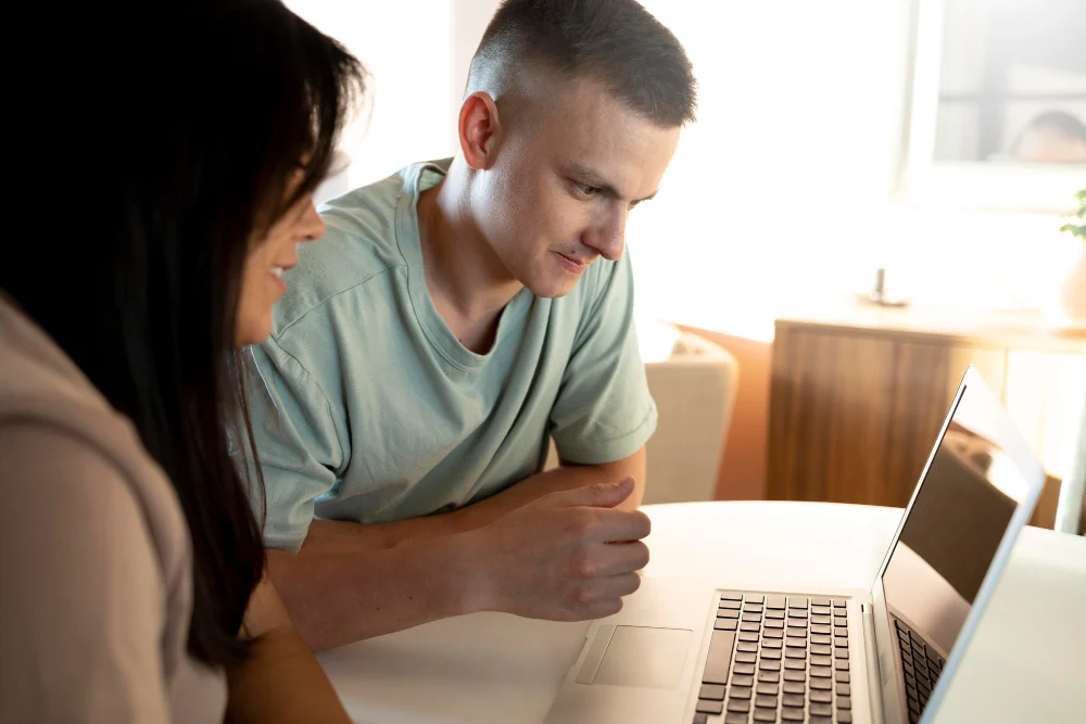 A man and woman looking at a laptop together at a table