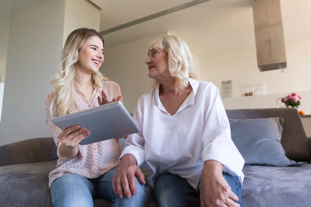 Woman sitting on couch with granddaughter discussing aged care Woman sitting on couch with granddaughter discussing aged care