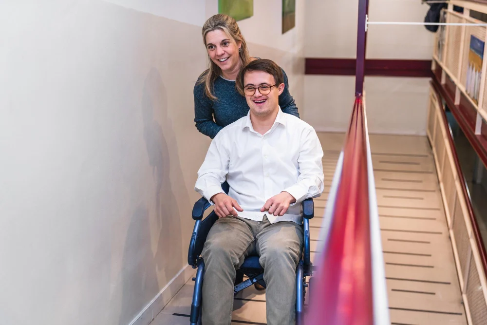 A woman assisting a man in a wheelchair on an indoor ramp