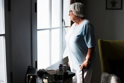 elderly woman in home looking out window