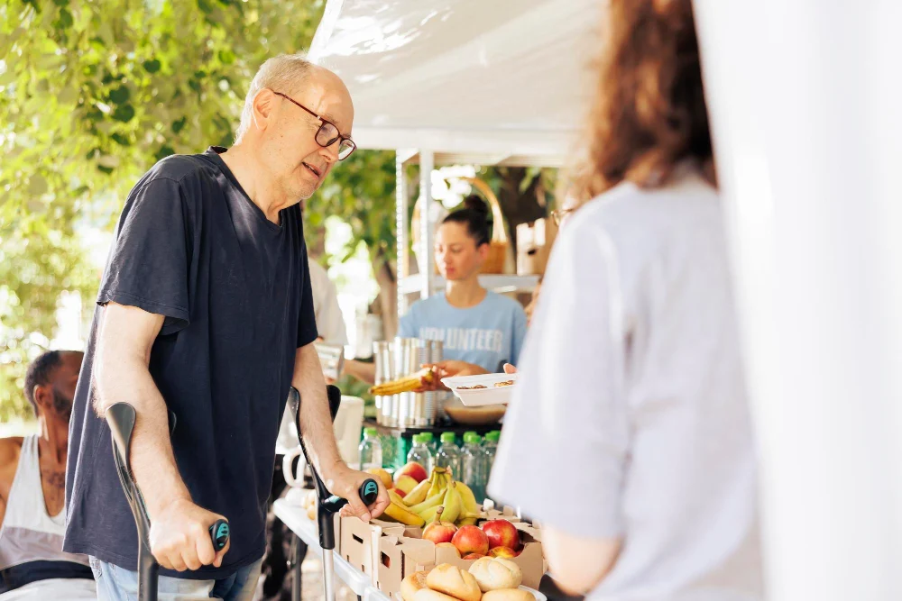 Man using crutches choosing food at an outdoor community market stall