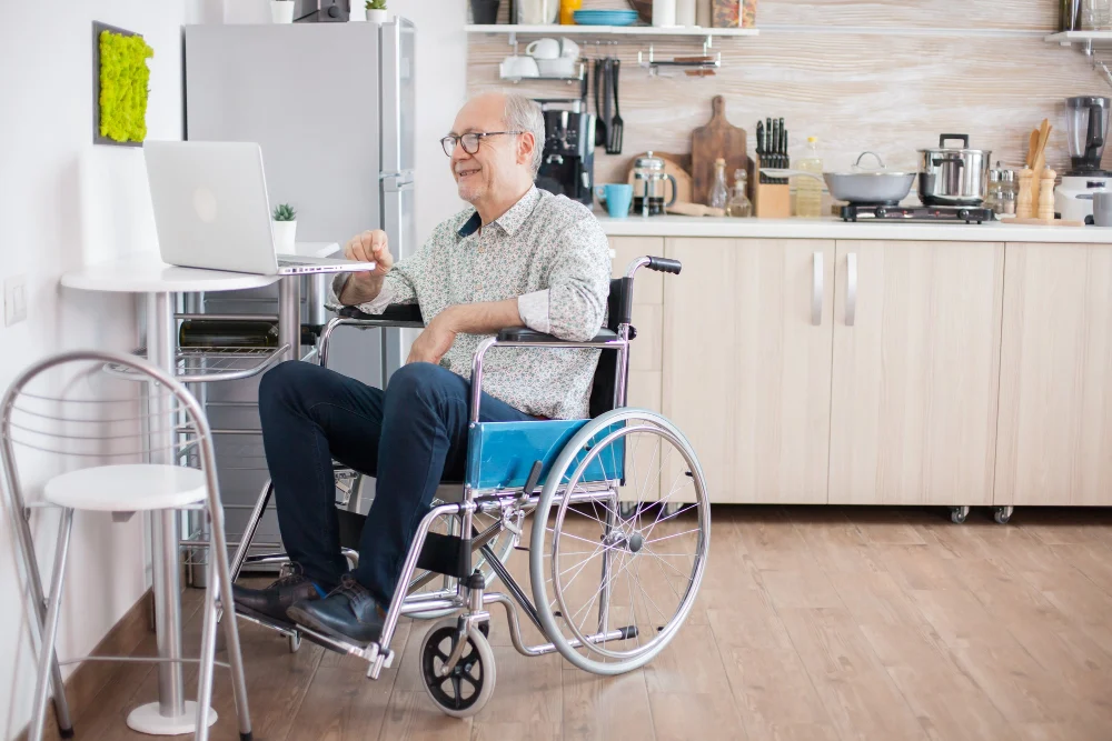 Man using a wheelchair independently accessing a laptop at home Man using a wheelchair independently accessing a laptop at home
