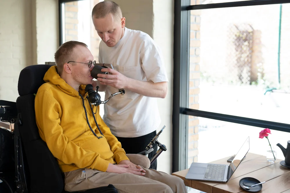 NDIS Work, Study and Disability-Related Health Supports Support worker assisting an NDIS participant with disability-related health support while using a laptop at home
