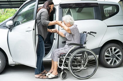 Support worker assisting an older wheelchair user into a car for transport