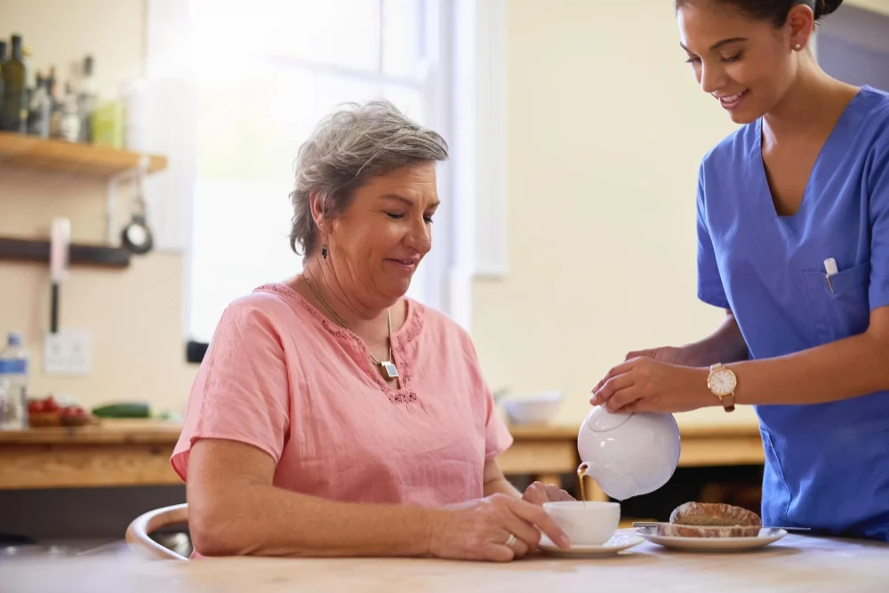 Support worker pouring tea for older woman at home