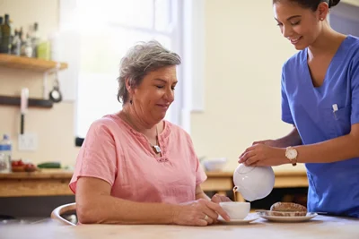 Support worker pouring tea for older woman at home