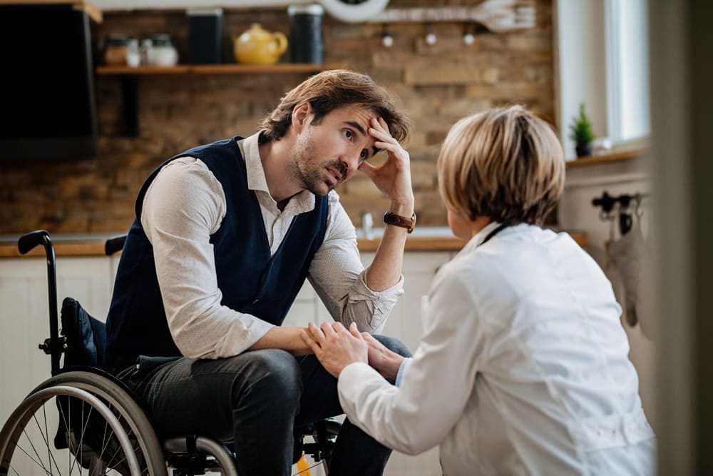 Young worried man in wheelchair communicating with support worker